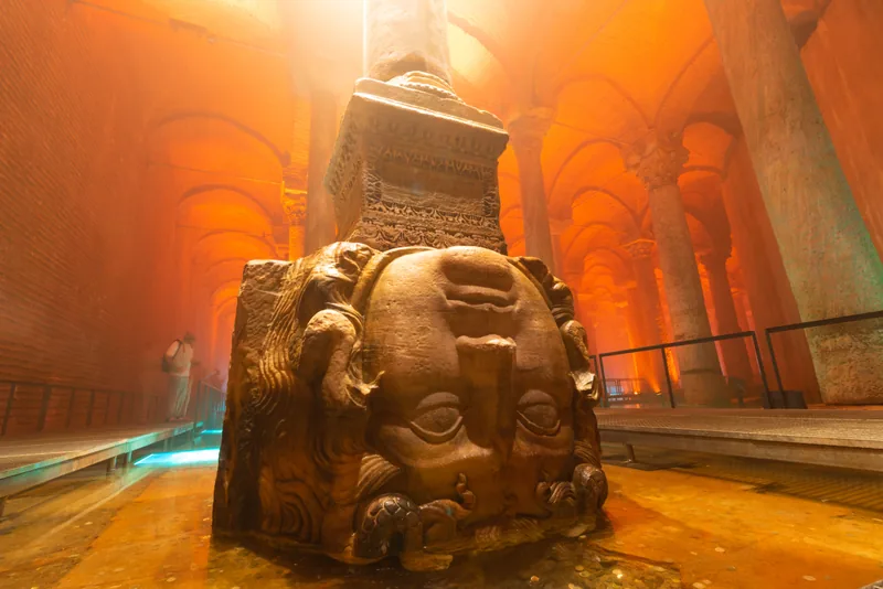 An upside-down Medusa head supporting a column inside Basilica Cistern, with its full carved face visible
